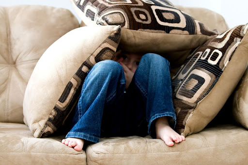 A child hiding under a stack of pillows feeling insecure.